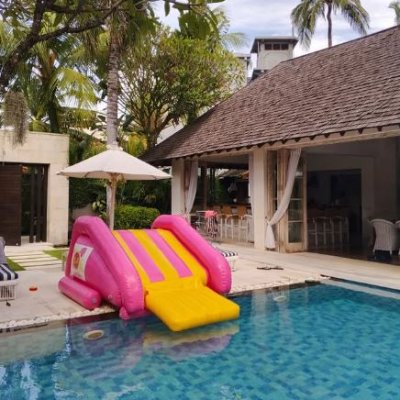 Family enjoying a large inflatable waterslide set up in a villa’s outdoor area, with kids playing and splashing in a safe, fun tropical environment.
