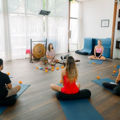 Participants engaging in sound healing and meditation in a tranquil tropical setting, using singing bowls and other instruments to promote relaxation and wellness.