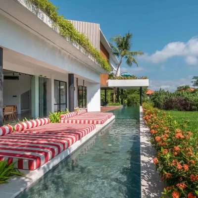 MandalaOasis_Bali_03_Pool_11zon A luxurious tropical villa named Mandala Oasis Villa, featuring an infinity pool surrounded by palm trees, lush gardens, and modern open-air architecture under a bright blue sky.
