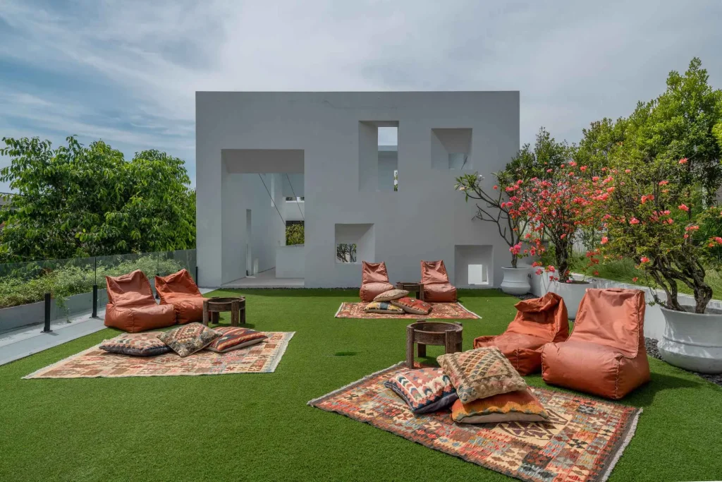 A luxurious tropical villa named Mandala Oasis Villa, featuring an infinity pool surrounded by palm trees, lush gardens, and modern open-air architecture under a bright blue sky.