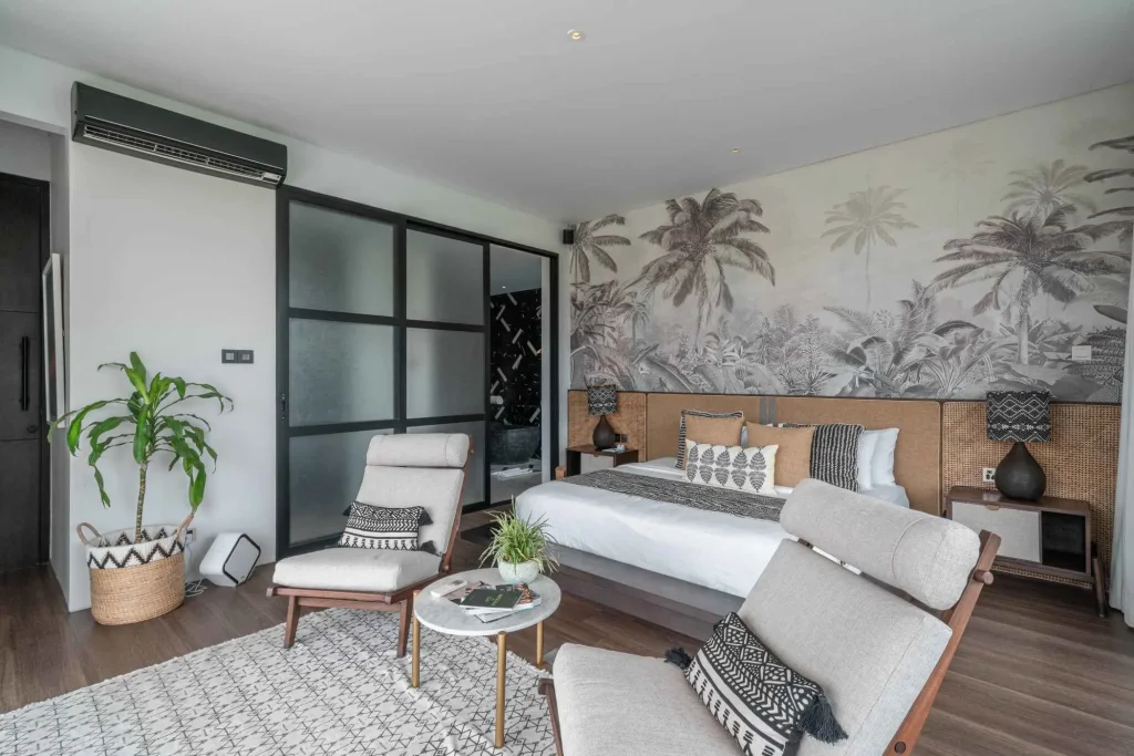 A luxurious tropical villa named Mandala Oasis Villa, featuring an infinity pool surrounded by palm trees, lush gardens, and modern open-air architecture under a bright blue sky.