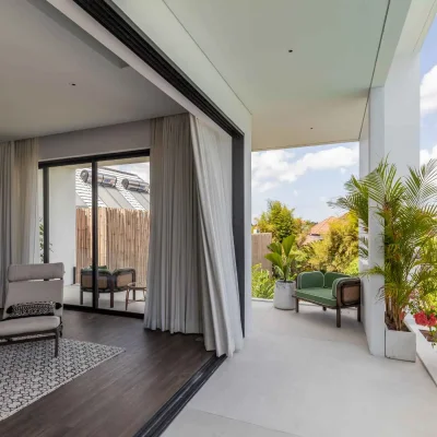 MandalaOasis_Bali_13_MasterBalcony_11zon A luxurious tropical villa named Mandala Oasis Villa, featuring an infinity pool surrounded by palm trees, lush gardens, and modern open-air architecture under a bright blue sky.