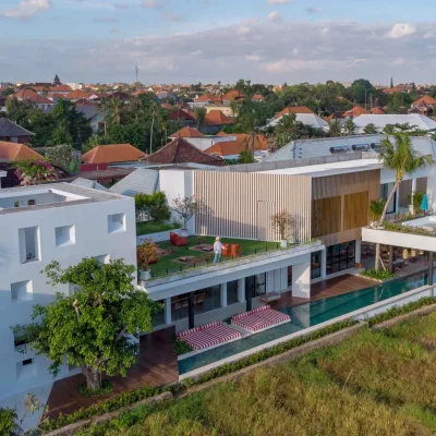 Mandala Oasis Villa A luxurious tropical villa named Mandala Oasis Villa, featuring an infinity pool surrounded by palm trees, lush gardens, and modern open-air architecture under a bright blue sky.