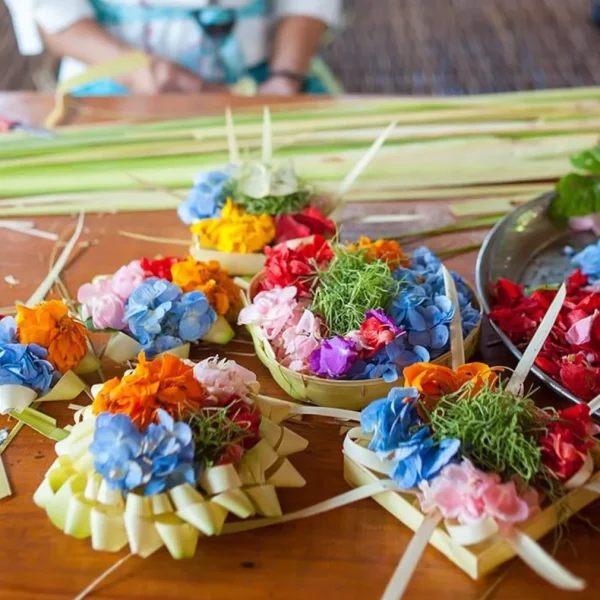 Workshop for making Balinese Canang Sari offerings, showing participants crafting small colorful floral arrangements used in daily Hindu rituals, set in a tropical setting.
