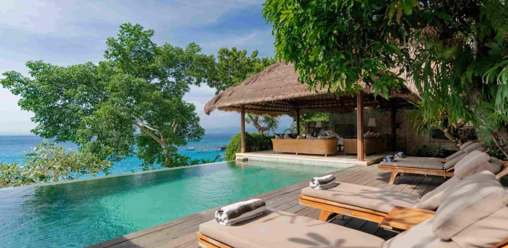 Spacious tropical villa named Villa Sayang Besar, featuring open-air living spaces, a large swimming pool, lush greenery, and traditional Balinese design elements